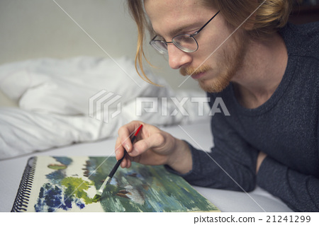 图库照片: young man lying in bed painting a picture