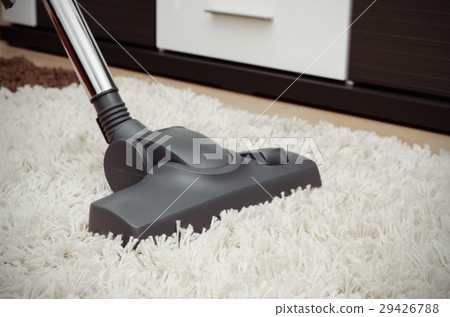 图库照片: vacuum cleaner cleans the white shaggy carpet.