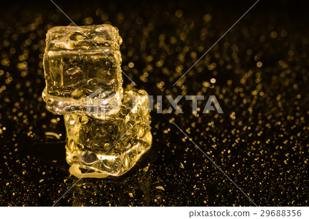 图库照片: ice cubes in yellow light on black wet table.