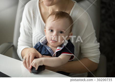 图库照片: cute baby boy sitting on mother lap while she work