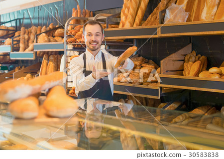 male shop assistant demonstrating delicious loaves of bread in