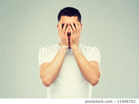 图库照片: man in white t-shirt covering his face with hands