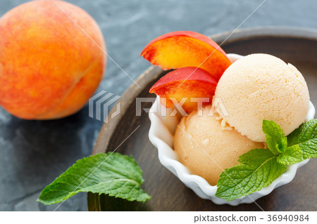 图库照片: peach ice cream and peach slices in a white bowl.