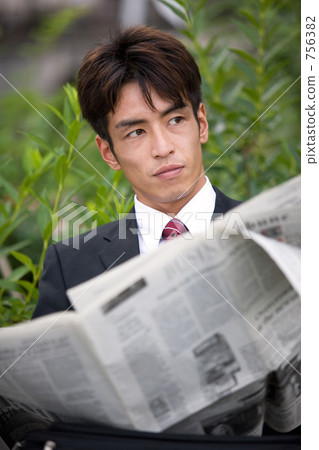 A businessman reading a newspaper on a park bench 756382