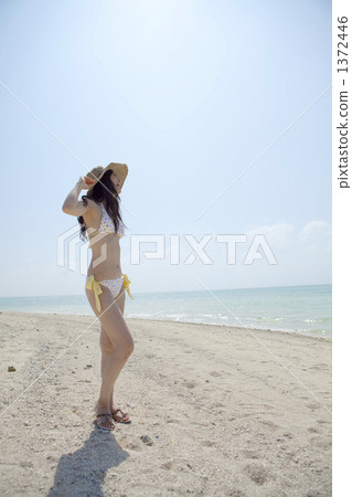站立在一個白色沙灘的泳裝婦女注視著天空 1372446