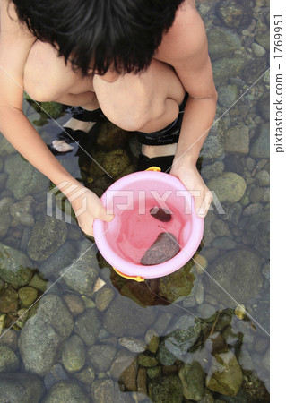 A girl looking over a bucket of a small fish caught in a river 1769951