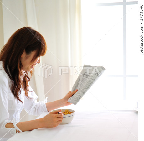 A woman reading a newspaper while eating breakfast 1773346