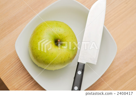 A cooking scene with a green apple and a knife on a plate. A cooking scene with a green apple and a knife on a plate. 2408417
