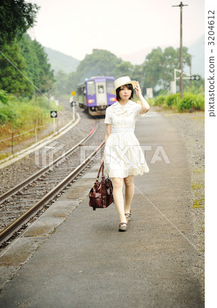 There is a train in the background at a lady station of a solo traveler 3204612