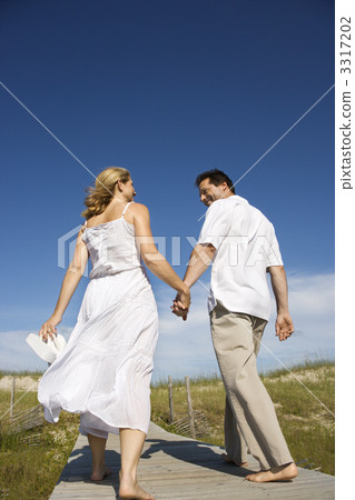 Couple holding hands walking down path. 3317202