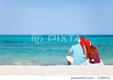 Romantic couple in Santa hats sitting on tropical beach Romantic couple in Santa hats sitting on tropical beach 3389411