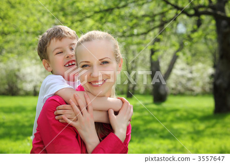 son embraces behind mother for neck in park in spring 3557647