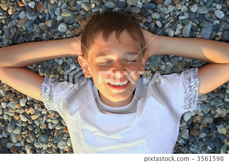teenager boy lying on stones on stone seacoast, closed eyes, hol 3561598