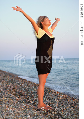 beautiful young woman lifted hands upwards on stone seacoast, fu 3561691