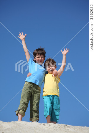Two boys stand on sand and lifted hands in greeting Two boys stand on sand and lifted hands in greeting 3562023