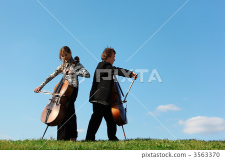 Two violoncellists play on grass against  sky 3563370