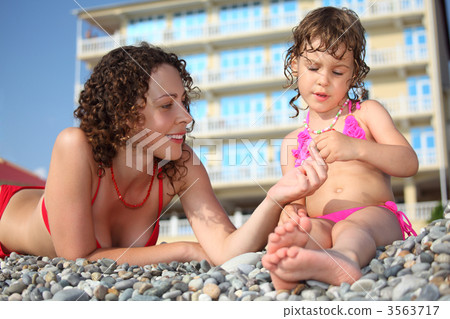 Mother with daughter on pebble in swimwear 3563717