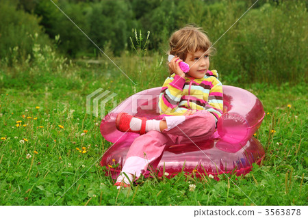 little girl sits talks by toy phone in inflatable armchair  on l 3563878