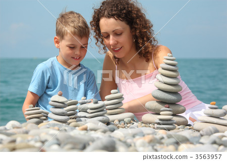 mother and son builds  stone stacks on pebble beach 3563957