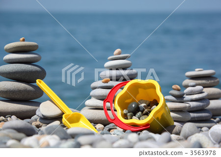 Yellow children's bucket with  scoop and stone stacks on seacoas 3563978