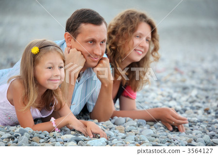 Happy family with little girl lying on stony beach 3564127