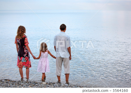 Happy family with little girl standing on beach in evening, stan Happy family with little girl standing on beach in evening, stan 3564160