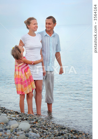 Happy family with little girl standing on beach in evening, look Happy family with little girl standing on beach in evening, look 3564164