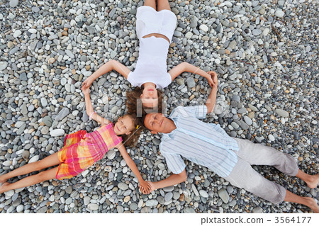 Happy family with little girl lying on stony beach, having joine 3564177