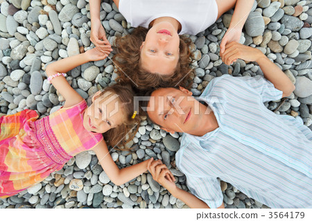 Happy family with little girl lying on stony beach, having joine 3564179