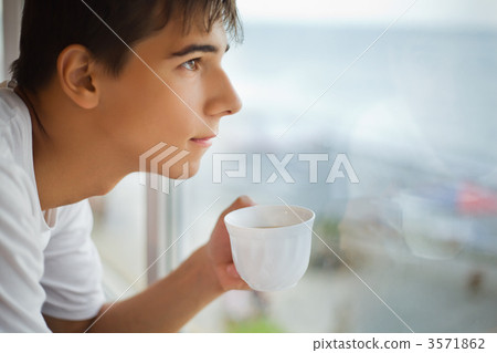 teenager boy with cup in hand looking out of window in morning, 3571862