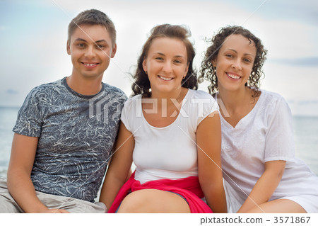 Smiling man and two young beautiful women sitting on beach Smiling man and two young beautiful women sitting on beach 3571867