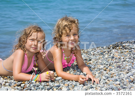 two pretty little girls lying on stony beach near sea two pretty little girls lying on stony beach near sea 3572161