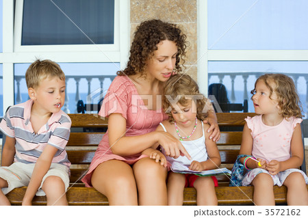 young beautiful woman reads book to two little girls and boy on young beautiful woman reads book to two little girls and boy on 3572162