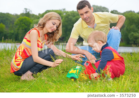 child sits on grass with parents and plays with toy child sits on grass with parents and plays with toy 3573250