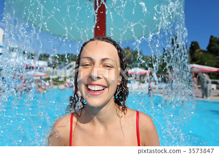 Smiling beautiful woman bathes in pool under water splashes, und 3573847