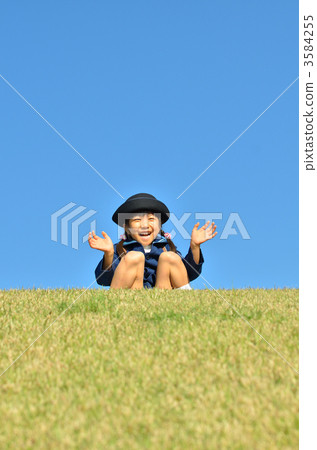 幼兒園的孩子（女孩）坐在草坪上，揮舞著一隻手 3584255