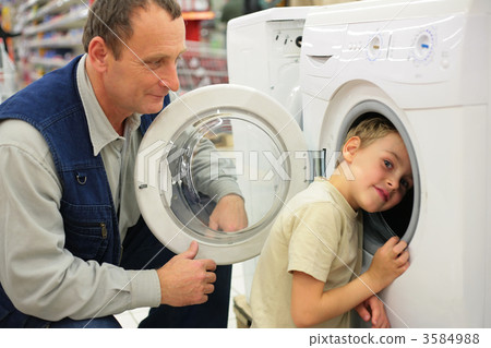 Man looks at washing machine in store, boy glances inward it. Man looks at washing machine in store, boy glances inward it. 3584988
