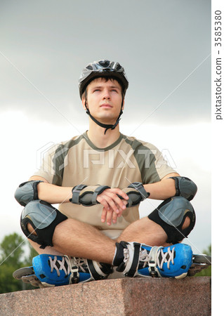 Boy on rollerblades sits with crossed legs 3585380