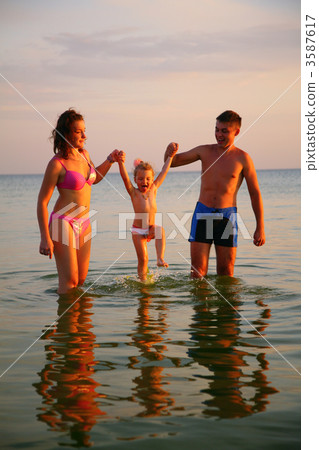 Parents hold daughter from hands in sea Parents hold daughter from hands in sea 3587617