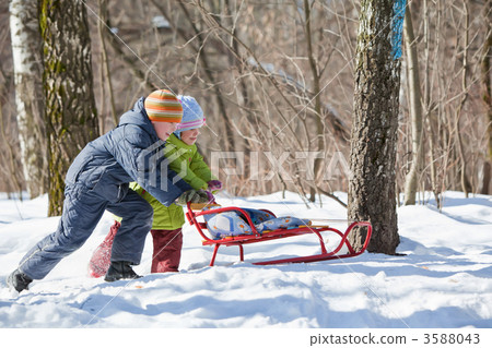 boy and little girl push sledge in winter in wood boy and little girl push sledge in winter in wood 3588043