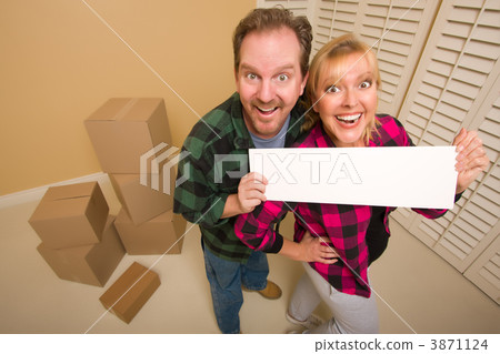 Happy Couple Holding Blank Sign in Room with Packed Boxes 3871124