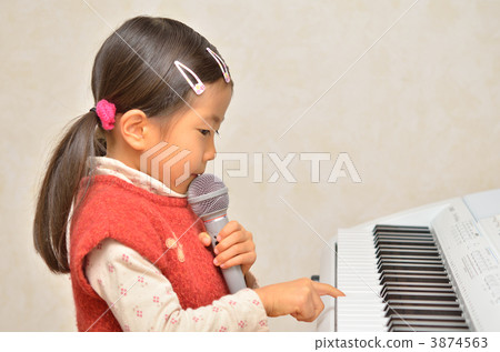 A girl playing the piano while singing with a microphone 3874563