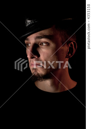 Low key studio portrait of young discontented man in hat over bl 4353158