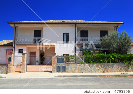Facade of fenced white two-story cottage with garden and balcony 4795596