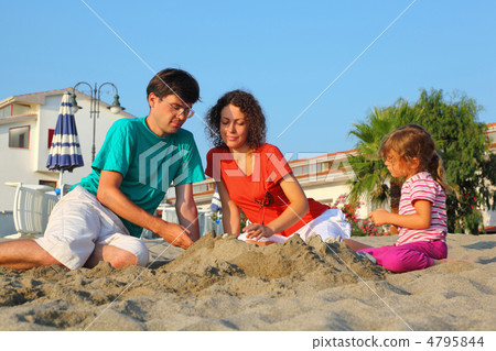Mother with father and girl sit in  day-time on  beach and build 4795844