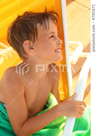 Cheerful little boy sits in yellow deck chair and wrap oneself u 4795871