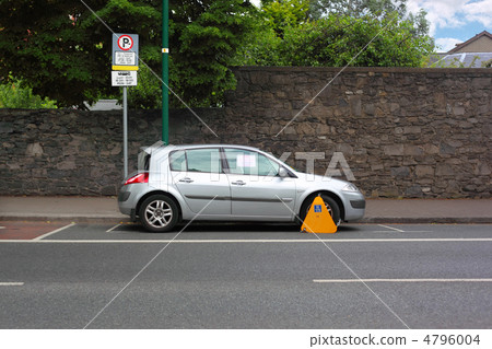 Car street clamped with yellow metal wheel clamp. Trees grow beh Car street clamped with yellow metal wheel clamp. Trees grow beh 4796004