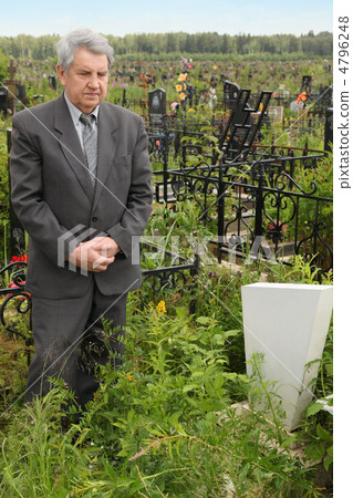 old sad senior in grey suit standing near grave with white grave 4796248