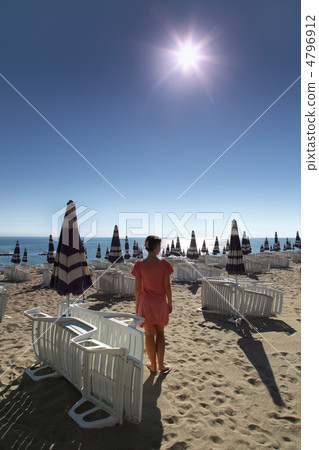Woman stands on sunny beach with sun loungers and umbrellas 4796912