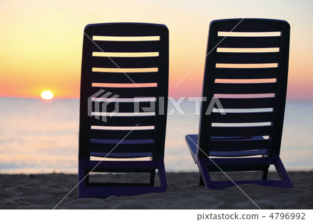 Two plastic chairs stand on  beach near water with  view on suns 4796992